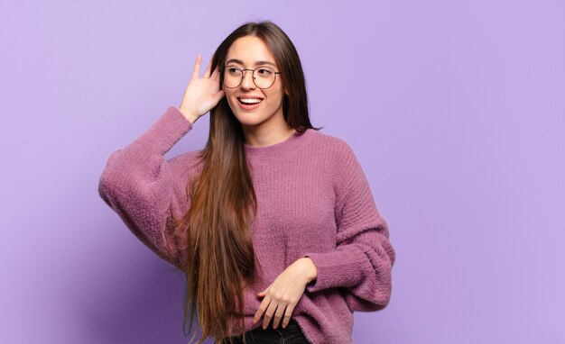 Jeune femme assez décontractée souriante, regardant curieusement sur le côté, essayant d'écouter des potins ou d'entendre un secret