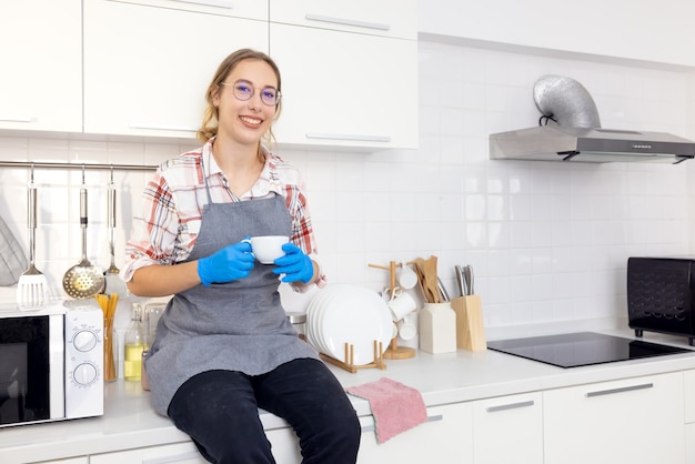 Jeune femme assez élégante tenant une tasse blanche dans une cuisine blanche après avoir serré, Jeune femme relaxante,