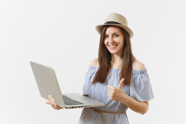 Jeune femme assez heureuse en robe bleue, chapeau travaillant sur ordinateur portable moderne isolé sur fond blanc. Entreprise indépendante, mode de vie, concept d'achat en ligne. Bureau mobile. Publicité