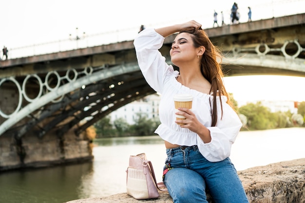 Jeune femme assise au bord de la rivière Fille avec un café à Séville Espagne Touriste en vacances d'été