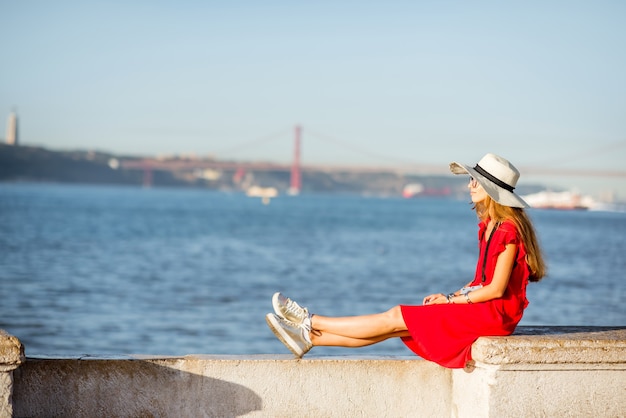 Jeune femme assise au bord de la rivière avec vue paysage sur le pont dans la ville de Lisbonne, Portugal