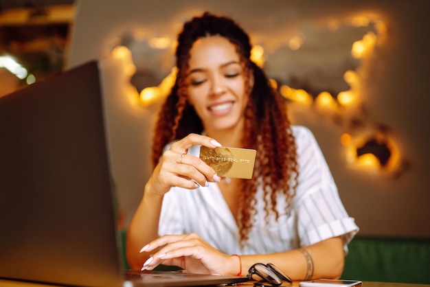 Jeune femme assise au café faisant des achats en ligne à l'aide d'une carte de crédit et d'un ordinateur portable