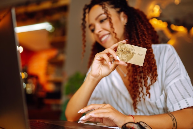 Jeune femme assise au café faisant des achats en ligne à l'aide d'une carte de crédit et d'un ordinateur portable