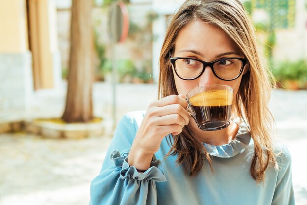 Jeune femme assise au café en plein air avec une tasse de café