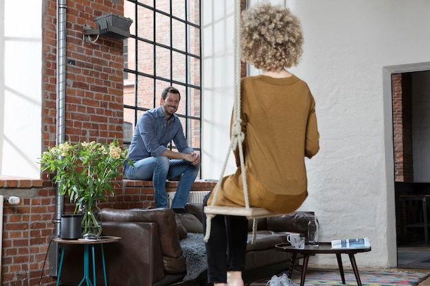 Photo jeune femme assise sur une balançoire dans le salon, parlant à l'homme