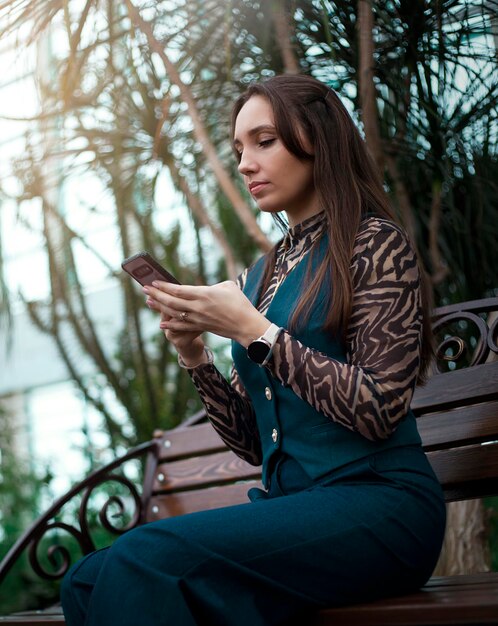 Photo une jeune femme assise sur un banc dans le parc et utilisant un smartphone