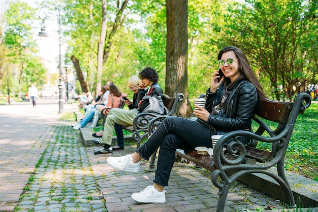 Jeune femme assise sur le banc dans le parc de la ville parlant par téléphone style de vie