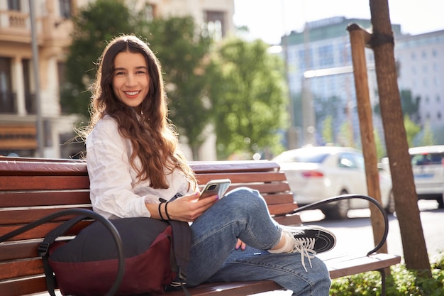 Jeune femme assise sur un banc dans la ville tout en utilisant son téléphone portable