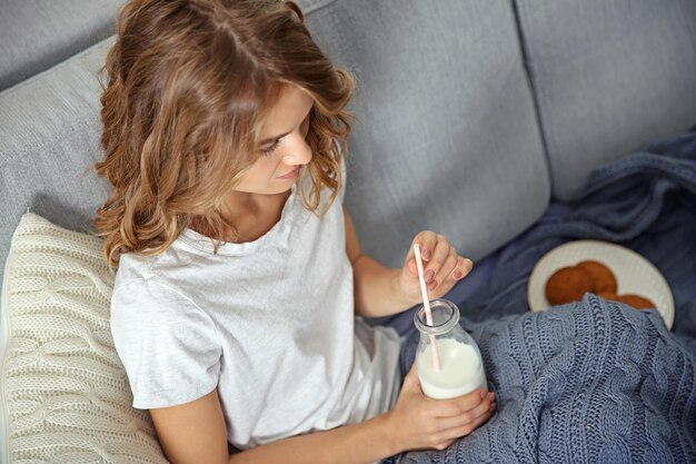 Jeune femme assise sur un canapé avec une bouteille de lait et des biscuits