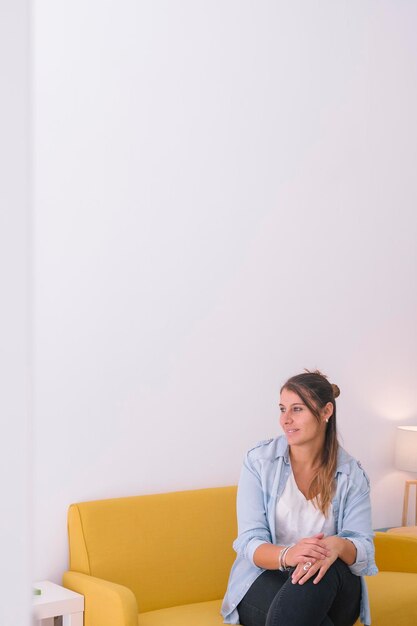 Une jeune femme assise sur le canapé contre le mur.