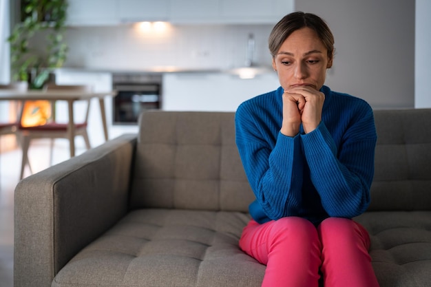 Jeune femme assise sur un canapé avec une expression déprimée et fatiguée après avoir rompu avec son petit ami