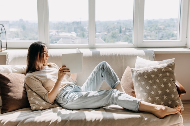 Jeune femme assise sur un canapé et lisant un livre