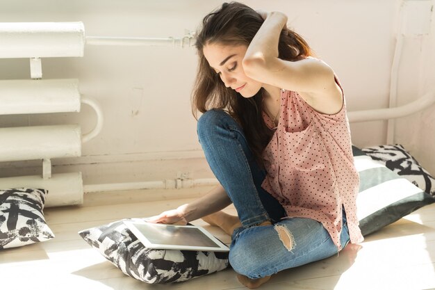 Jeune femme assise sur un canapé et regarder la tablette ou surfer sur le net et souriant