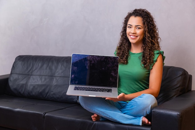 Jeune femme assise sur un canapé tenant un ordinateur portable avec un écran vide vide avec un espace pour le texte.