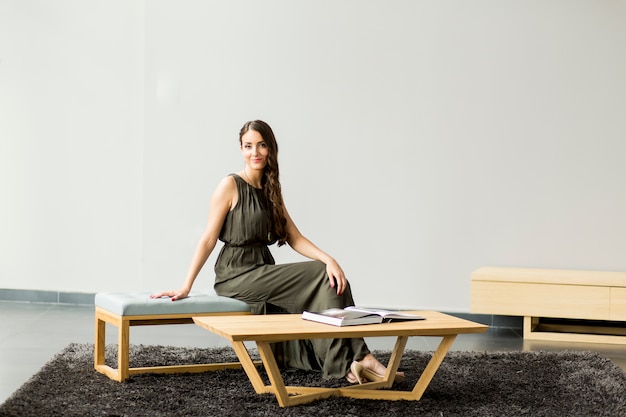 Jeune femme assise sur la chaise dans la chambre avec un livre sur les jambes