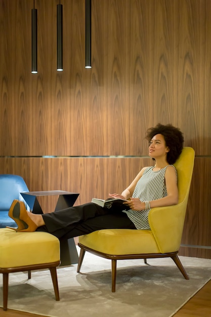 Jeune femme assise sur une chaise jaune et lisant un livre