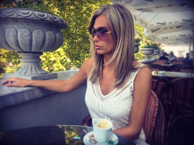 Photo une jeune femme assise à côté du café sur une chaise.