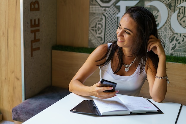Jeune femme assise dans un café à table et tapant un message sur le smartphone, un blogueur d'âge moyen prend...