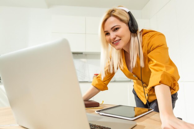 Jeune femme assise dans la cuisine et travaillant sur ordinateur portable.