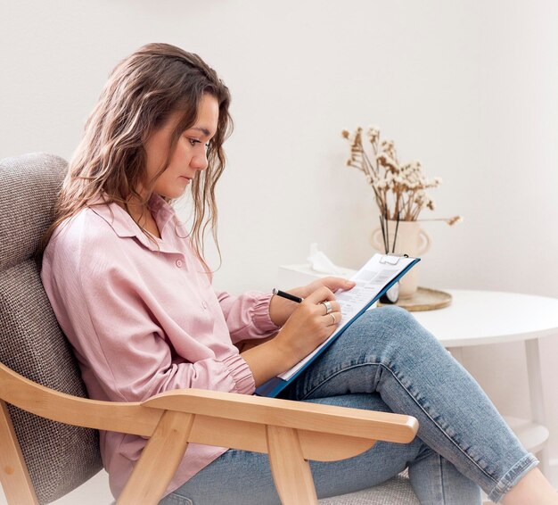 Jeune femme assise dans un fauteuil et écrivant dans un carnet à la maison