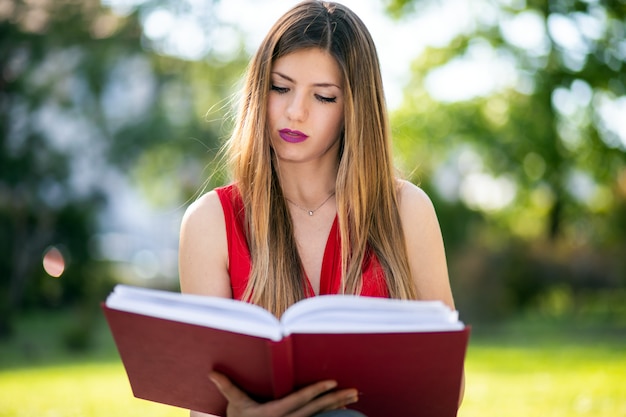 Jeune femme assise dans un parc et lisant un livre