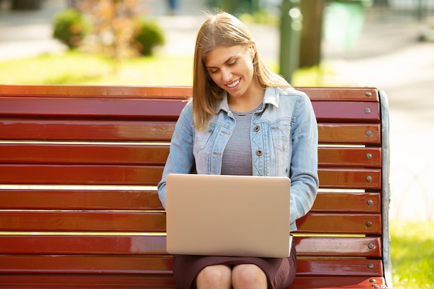 Jeune femme assise dans le parc et travaillant avec un ordinateur portable