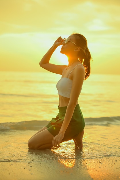 Photo jeune femme assise dans le sable à la mer au coucher du soleilfemme profitant de la plage relaxante joyeuse en été avec le coucher du soleil