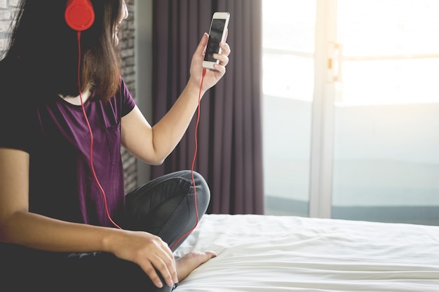 Jeune femme assise dans son lit et écoute de la musique dans sa chambre à coucher à la maison de détente