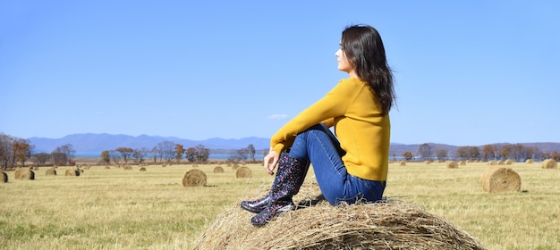 Jeune femme assise sur le dessus de la botte de foin dans le champ et à l'écart