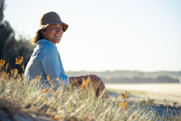 Jeune femme assise entre l'herbe dans une plage pointant vers l'horizon contre Clear SkyCopy Space