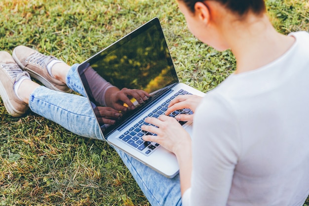 Photo jeune femme assise sur l'herbe verte avec son ordinateur portable