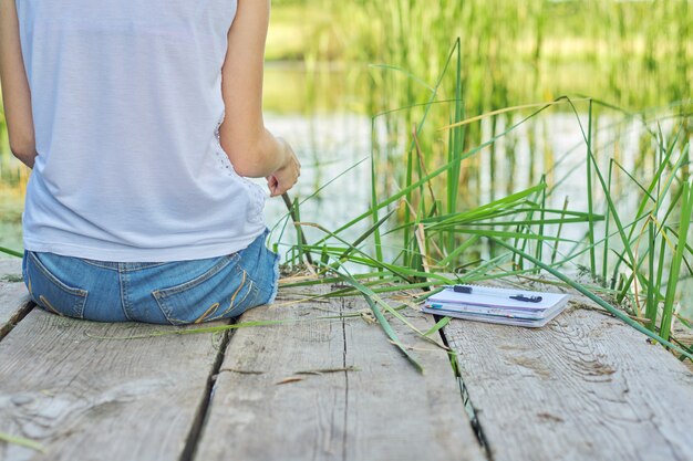 Jeune Femme Assise Sur Une Jetée En Bois, Bénéficiant D'une Vue Pittoresque Sur L'eau Du Lac