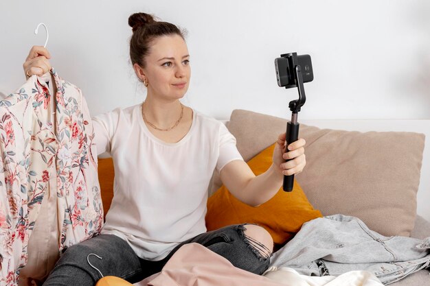 Jeune femme assise sur le lit à la maison et prenant une photo de ses vieux vêtements pour les vendre en ligne