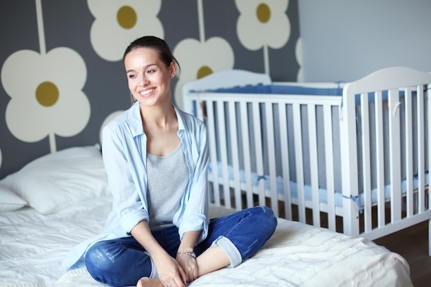 Jeune femme assise sur le lit près du lit d'enfant