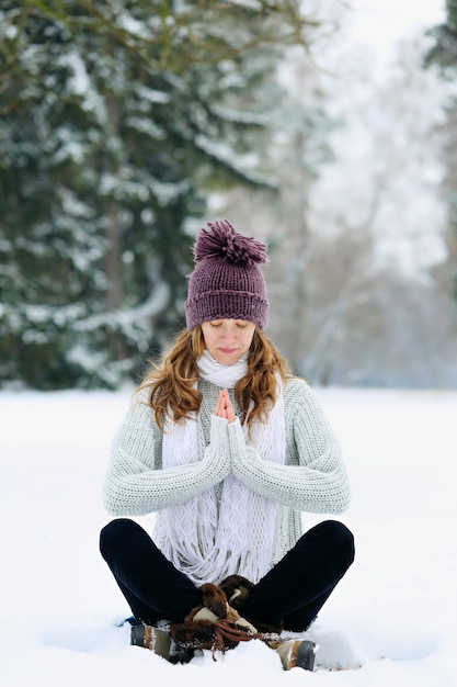 Jeune femme assise et méditant dans le parc en hiver