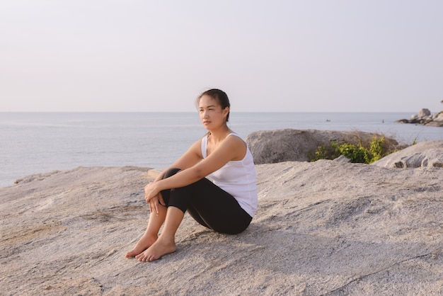 Jeune femme assise à la mer au lever du soleil