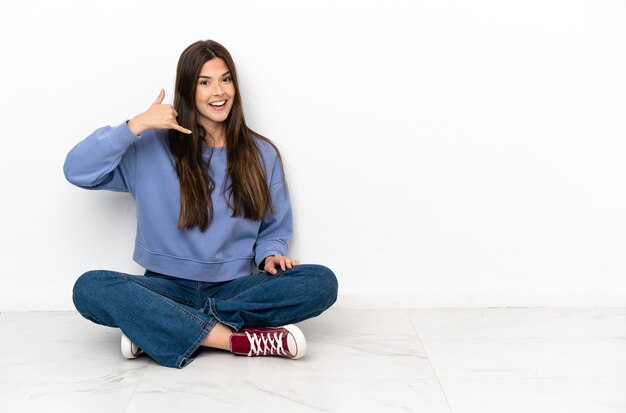 Jeune femme assise par terre faisant un geste de téléphone. Rappelle-moi signe