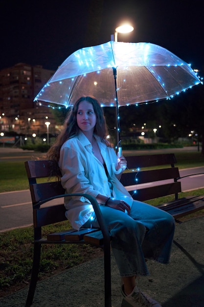 Jeune femme assise avec un parapluie avec des lumières la nuit