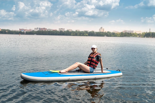 Jeune femme assise sur une planche à pagaie porter un gilet de sauvetage et apprendre à nager mode de vie actif d'été