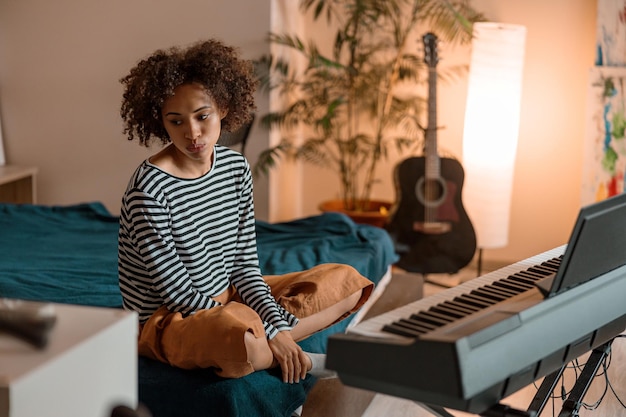 Jeune femme assise près du synthétiseur à la maison