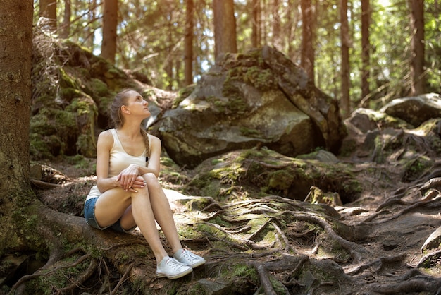 Jeune femme assise sur les racines des arbres dans la forêt sauvage. Forêt de conte de fées et blanc neige moderne.