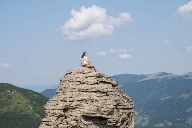 Jeune femme assise sur un rocher en montagne alrea rural sur la journée d'été ensoleillée et bénéficie de beaux paysages