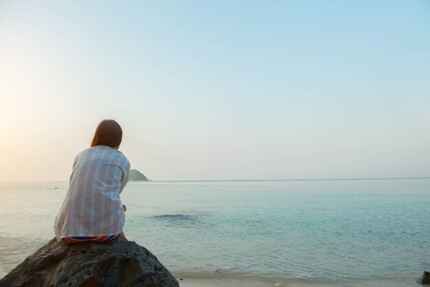 Jeune femme assise sur un rocher profitant de la plage et de la mer