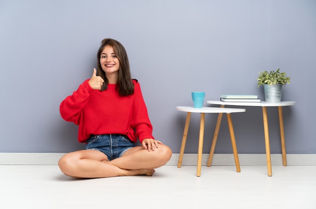 Jeune femme assise sur le sol, donnant un geste du pouce levé