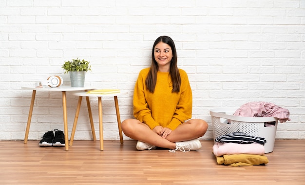 Jeune femme assise sur le sol à l'intérieur avec panier de vêtements penser une idée tout en levant