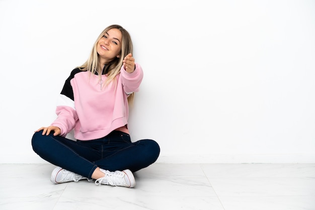 Jeune femme assise sur le sol à l'intérieur se serrant la main pour conclure une bonne affaire