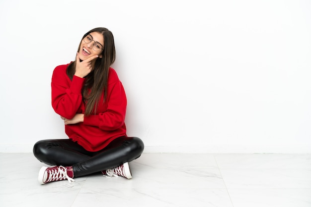 Jeune femme assise sur le sol isolé sur fond blanc souriant