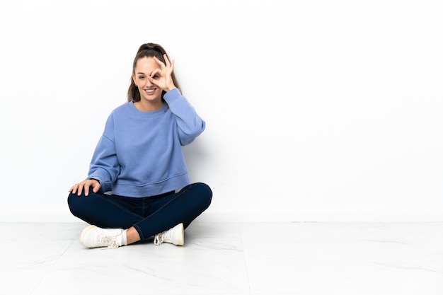 Jeune femme assise sur le sol montrant signe ok avec les doigts