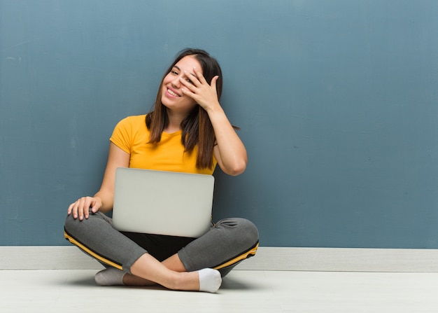 Jeune femme assise sur le sol avec un ordinateur portable embarrassé et riant en même temps