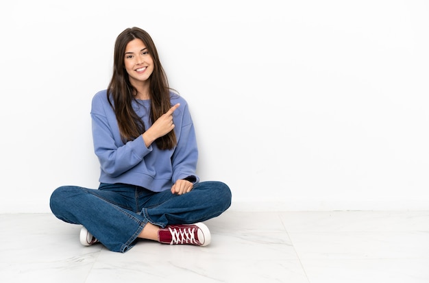 Jeune femme assise sur le sol pointant vers le côté pour présenter un produit